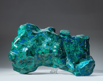 May include: A large, irregularly shaped piece of malachite with a swirling pattern of green and blue. The stone has a smooth, polished surface.