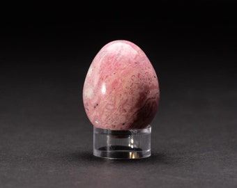 May include: A pink and white polished gemstone egg on a clear acrylic stand. The egg has a swirling pattern of pink and white.