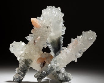 May include: A cluster of white, clear, and light pink quartz crystals with a grey, green, and black base. The crystals are clustered together in a natural formation.