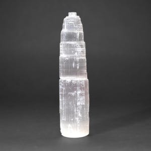 Op de afbeelding: Een witte seleniet torenkristal met een gelaagde, puntige top. De kristal is glad en doorschijnend.