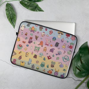 May include: Laptop sleeve featuring a colorful pattern of whimsical cartoon creatures on a pastel rainbow background. The sleeve has a black border and a zipper closure. The laptop is partially visible inside the sleeve.