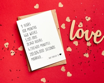 Puede incluir: Una tarjeta blanca con texto negro sobre un fondo rojo con confeti dorado y un letrero de madera que dice "love". La tarjeta dice "9 años, 108 meses, 468 semanas, 3.285 días, 78.840 horas, 4.730.400 minutos, 283.824.000 segundos, casados... y para siempre".