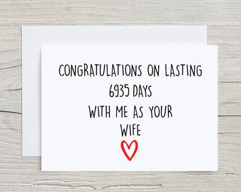 Puede incluir: Tarjeta blanca con texto negro que dice "Felicidades por durar 6935 días conmigo como tu esposa" y un corazón rojo.