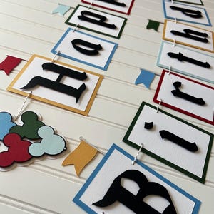 May include: A colorful banner with the words "Happy Birthday" in black letters on white squares with different colored borders. The banner is strung with white twine and has small flags with different colors.