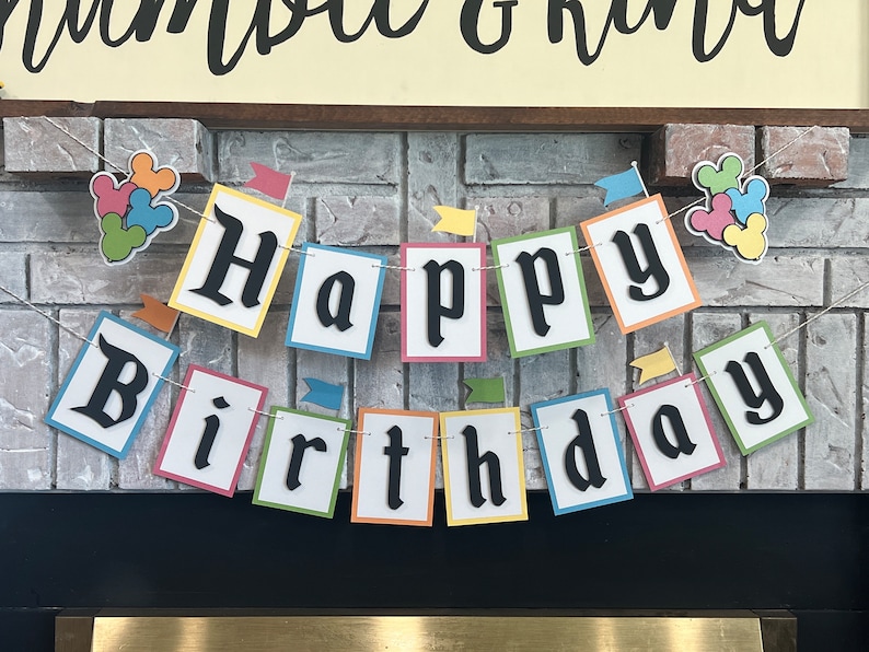 May include: A colorful banner with the words "Happy Birthday" in black letters on white squares. Each square has a different colored border. The banner is strung with a white string and has small flags hanging from it.