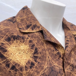 Op de afbeelding: Een bruin overhemd met knopen en een geometrisch patroon in tinten goud en bruin.