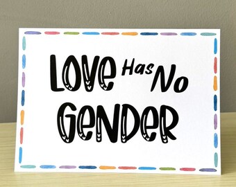 May include: A white rectangular card with the text "Love Has No Gender" in black, outlined with a colorful border. The card is displayed on a light wooden surface.