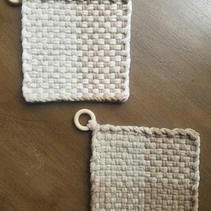 May include: Two woven pot holders with a wooden ring handle. The pot holders are made of a beige and white woven fabric.