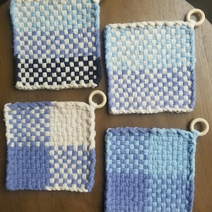 May include: Four woven pot holders with a checkered pattern in shades of blue, white, and black. Each pot holder has a wooden ring attached to the top corner.
