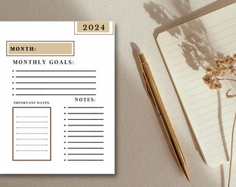 May include: A white 2024 monthly planner with sections for goals and notes. A gold pen and a small notebook with lined pages are next to the planner. A dried flower adds a decorative touch.