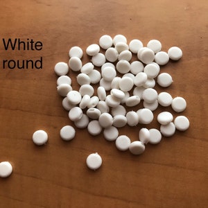 May include: A pile of white round plastic buttons. The buttons are about 1/2 inch in diameter.