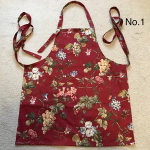 May include: A burgundy apron with a floral design of pink, blue, and cream flowers and green leaves. It has two pockets and long ties. The text "No.1" is visible in the upper right corner.