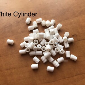 May include: A pile of white plastic cylinder cord ends.