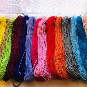 May include: A collection of 12 spools of colorful elastic cord. The colors are yellow, beige, green, burgundy, navy blue, lavender, pink, red, orange, gray, light blue, and peach.