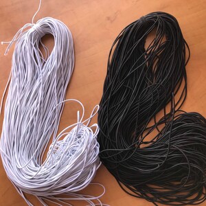 May include: Two spools of elastic cord, one white and one black. The spools are on a wooden surface.