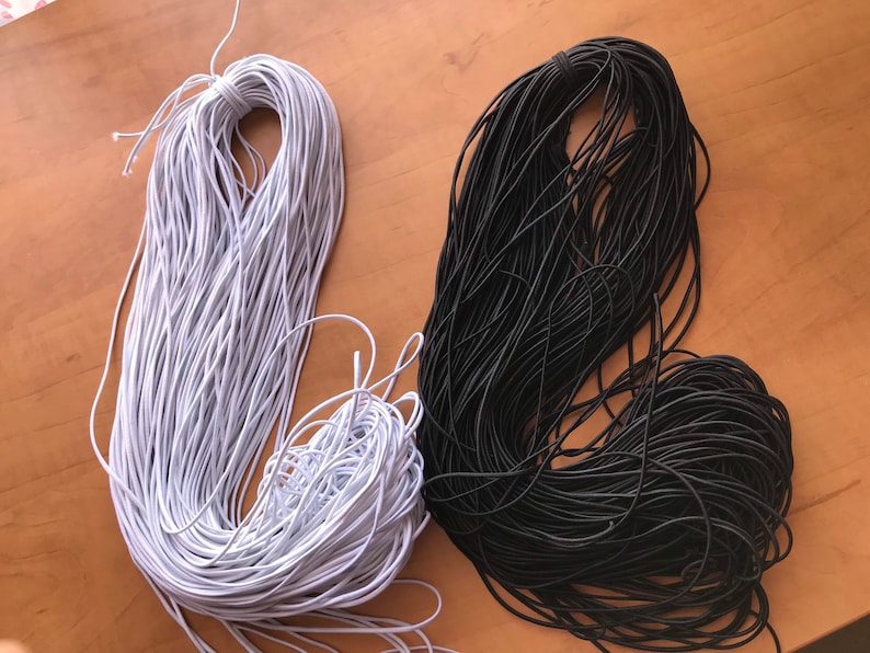 May include: Two spools of elastic cord, one white and one black. The spools are on a wooden surface.