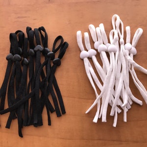 May include: A set of 10 black and 10 white elastic mask extenders with adjustable toggles. The toggles are heart-shaped on the black extenders and round on the white extenders.