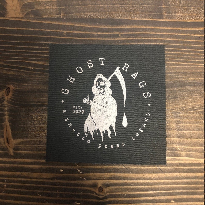 May include: Black and white patch featuring a Grim Reaper holding a scythe. The text surrounding the Grim Reaper reads "G. Ghost Rags. A Ghetto Press Legacy. Est. 2020."