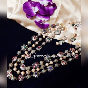 May include: An elaborate jewellery set comprising a multi-strand necklace, earrings, and a bracelet. The necklace and bracelet feature pearl beads and decorative silver floral accents with red, green, blue, and turquoise gemstones. The text "Specialjeweller india" is visible.