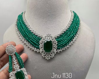 May include: A green beaded necklace and matching earrings set. The necklace features a large emerald-cut green stone pendant surrounded by a floral design. The earrings have a similar design. The text "Jnu 1130" is visible.