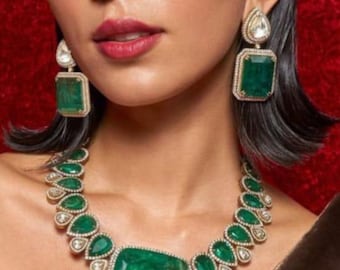 May include: A gold necklace with a large emerald green gemstone pendant surrounded by smaller emerald green gemstones and diamonds. The necklace is paired with matching emerald green and diamond earrings.