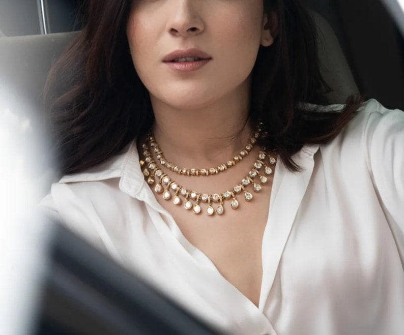 Puede incluir: Una mujer con una camisa blanca y un collar de oro y diamantes. El collar tiene dos hileras de peque&ntilde;os diamantes redondos y una hilera de diamantes redondos m&aacute;s grandes que cuelgan de la parte inferior.