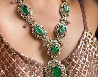 Può includere: Una collana d'oro con un grande ciondolo di pietra preziosa verde smeraldo e pietre preziose verdi smeraldo più piccole lungo la catena. La collana è decorata con intricati dettagli di diamanti.