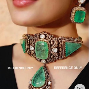 May include: A gold choker necklace with a large emerald green gemstone and smaller diamonds. The necklace has a pendant with a teardrop-shaped emerald green gemstone and diamonds. The necklace is on a model's neck. REFERENCE ONLY.