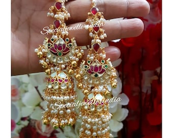 May include: A pair of gold earrings with pearl and gemstone embellishments. The earrings feature a crescent moon design with a lotus flower in the center. The earrings are adorned with red, green, and white gemstones. The earrings are also decorated with a string of pearls.