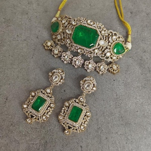 May include: A gold choker necklace with a large emerald green gemstone and smaller white gemstones. Matching earrings with emerald green gemstones and white gemstones.