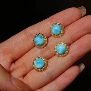 May include: Three gold earrings with blue gemstone cabochons. The earrings have a delicate, ornate design around the stones.