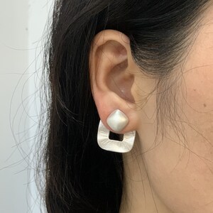 May include: Silver earrings with a square-shaped top and a geometric, open-frame design.