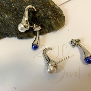 May include: A pair of silver earrings with a pearl and a blue gemstone. The earrings are shaped like a curved stem.