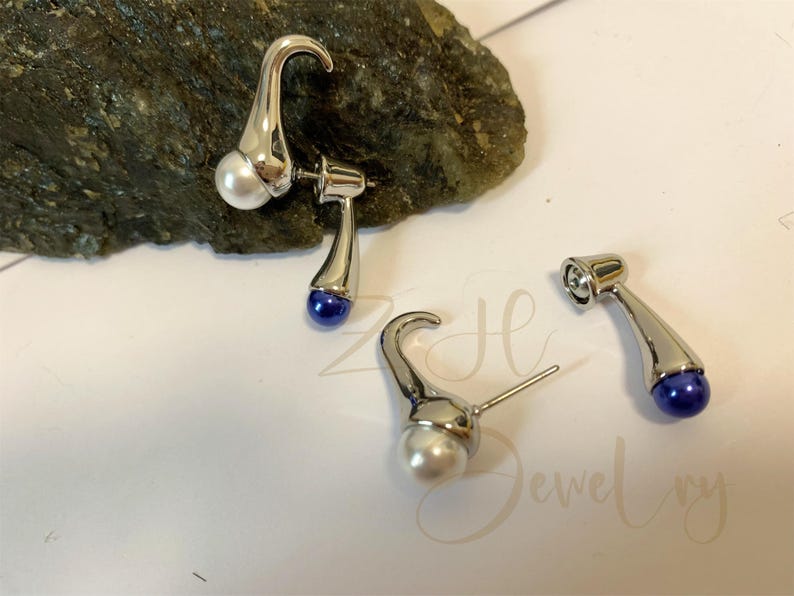 May include: A pair of silver earrings with a pearl and a blue gemstone. The earrings are shaped like a curved stem.