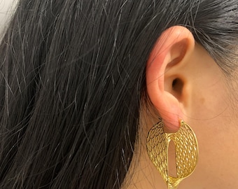 May include: Gold-toned earrings with a unique, openwork design. The earrings feature a wing-like shape with intricate detailing, creating a delicate and elegant aesthetic. The earrings are worn on the ear.