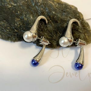 May include: A pair of silver earrings with a white pearl and a blue gemstone on each earring.