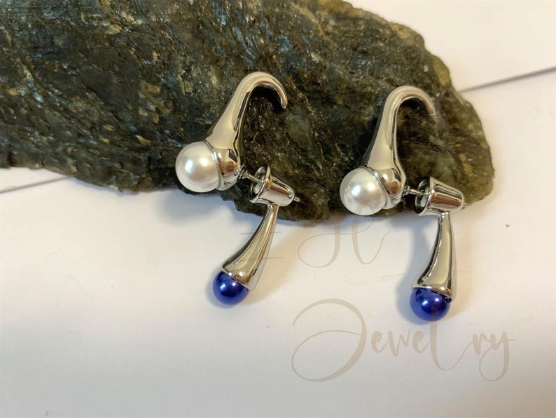 May include: A pair of silver earrings with a white pearl and a blue gemstone on each earring.