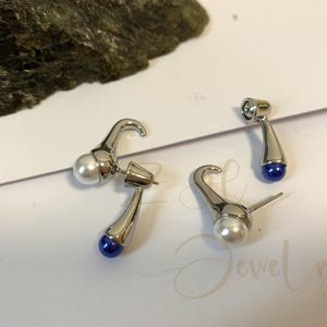 May include: A pair of silver earrings with a white pearl and a blue gemstone. The earrings are shaped like a curved hook.