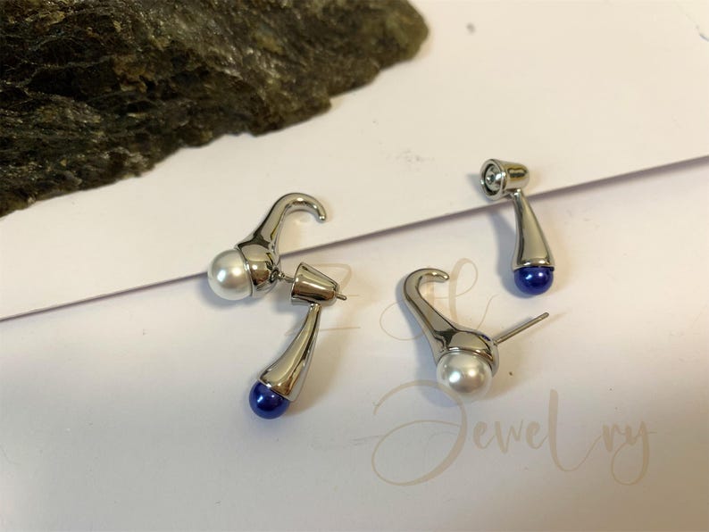 May include: A pair of silver earrings with a white pearl and a blue gemstone. The earrings are shaped like a curved hook.