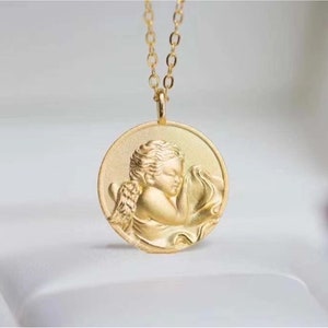 Pu&ograve; includere: Collana d'oro con un ciondolo rotondo che presenta una scultura a rilievo dettagliata di un angelo cherubino addormentato.