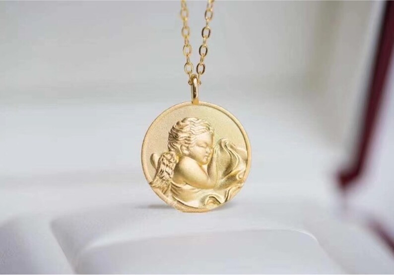 Pu&ograve; includere: Collana d'oro con un ciondolo rotondo che presenta una scultura a rilievo dettagliata di un angelo cherubino addormentato.