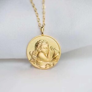 Pu&ograve; includere: Collana d'oro con un ciondolo rotondo che presenta un rilievo dettagliato di un angelo addormentato con le ali.