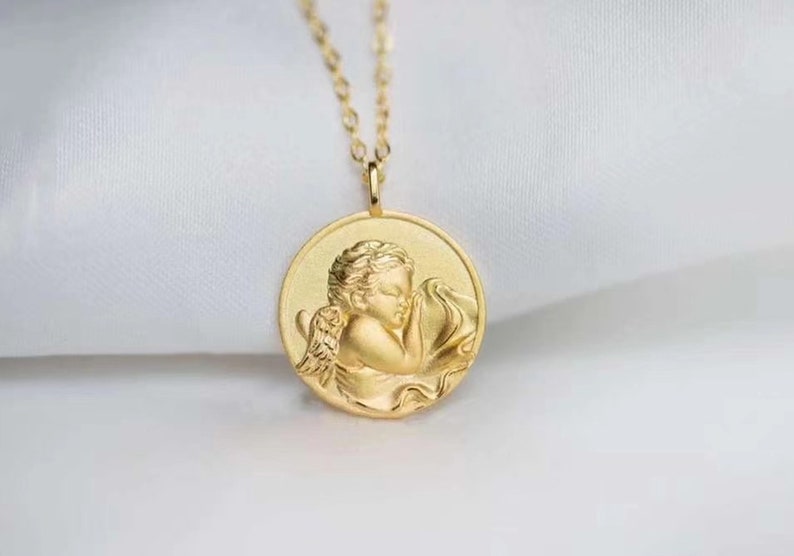 Pu&ograve; includere: Collana d'oro con un ciondolo rotondo che presenta un rilievo dettagliato di un angelo addormentato con le ali.