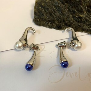 May include: A pair of silver earrings with a white pearl and a blue pearl on each earring.