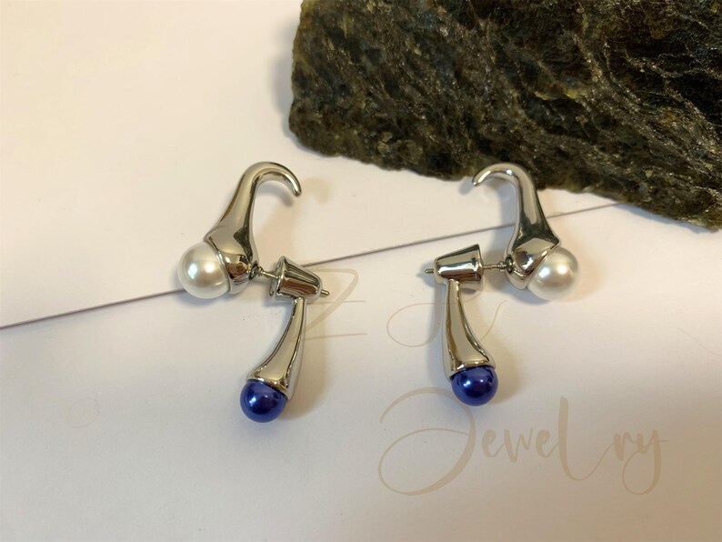 May include: A pair of silver earrings with a white pearl and a blue pearl on each earring.