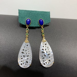 Puede incluir: Un par de pendientes largos de oro con piedras azules y verdes. Los pendientes tienen un colgante blanco en forma de lágrima tallado.