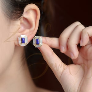 May include: A pair of gold earrings with a blue stone and white mother-of-pearl accents. The earrings are square shaped and have a geometric design.