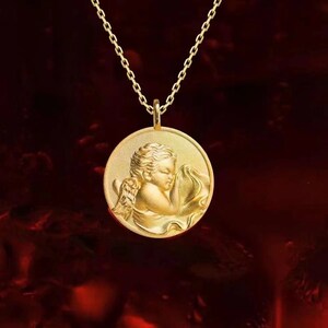 Pu&ograve; includere: Una collana d'oro con un ciondolo rotondo che presenta una scultura dettagliata di un angelo addormentato. L'angelo &egrave; raffigurato con ali e una veste fluida.