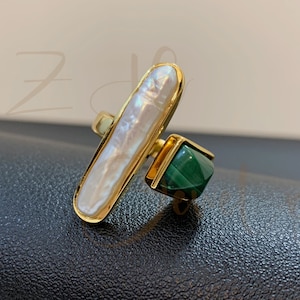 May include: Gold ring featuring a white pearl and a green malachite stone.