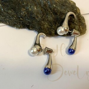 May include: A pair of silver earrings with a white pearl on one side and a blue pearl on the other side.